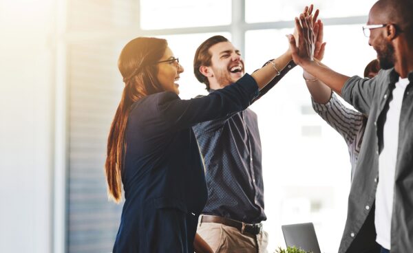 Un equipo de trabajo diverso celebrando con un gesto de 'high five' en una oficina moderna y luminosa, representando el concepto de employee engagement.