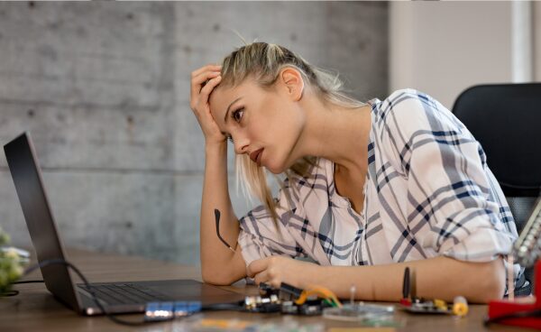 Mujer joven mirando una computadora portátil con gesto de cansancio, reflejando estrés y desmotivación en el entorno laboral.